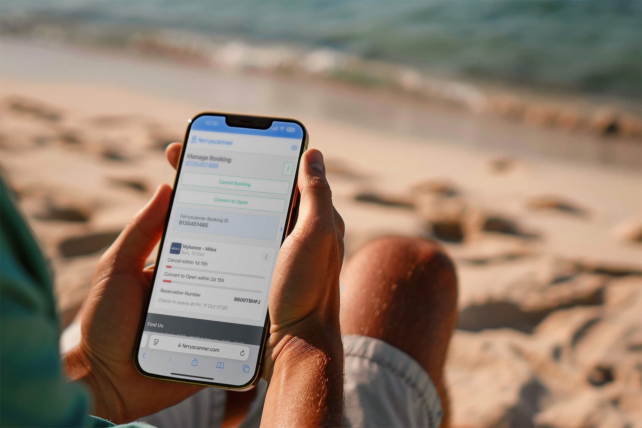 Henkilö, joka pitää kädessään älypuhelinta, jossa näkyy Ferryscanner "Hallinnoi varaustasi" -sivu samalla kun istuu hiekkarannalla meren äärellä. Tämä kuvastaa helppoutta hallita laivavarauksia missä ja milloin tahansa.