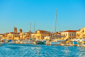 White houses with red onions on their roofs next to the harbour with clear blue waters and moored boats illuminated by the setting sun