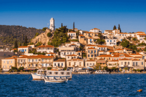 White houses and buildings with red onions on their roofs next to the blue waters of the sea with a few boats floating in it as the sun embraces them with its rays