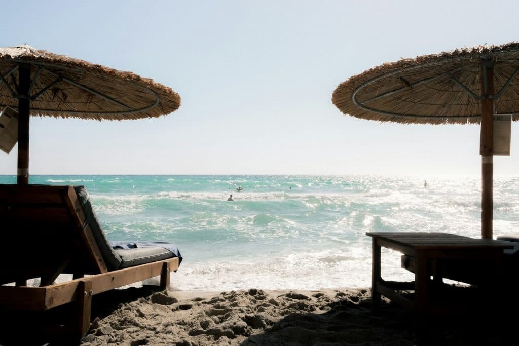 Two chairs under umbrellas sit next to eachother, facing the sea in Milos, Greece.