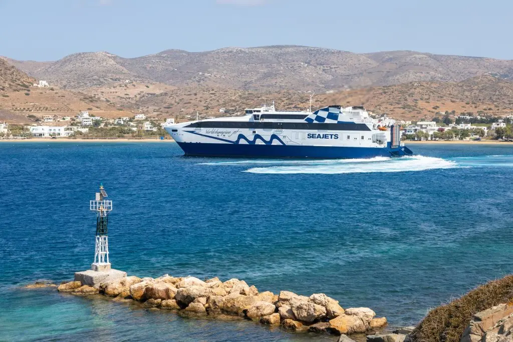 Εικόνα που απεικονίζει το Νέο Λιμάνι της Ίου, με ένα ταχύπλοο πλοίο της Seajets να πλέει στα καταγάλανα νερά και την παραθαλάσσια περιοχή στο βάθος.